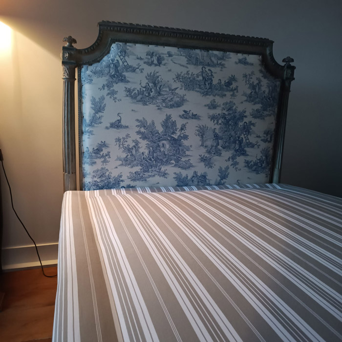 Sommier tapissier rayé fait sur mesure, au pied d’une tête de lit ancienne