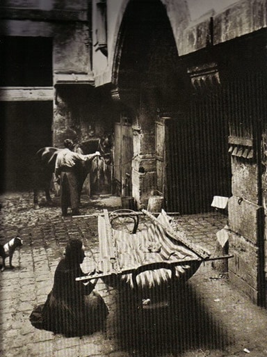 Old photograph: a woman mattress maker at work in a cobbled courtyard, a mattress stretched on its frame